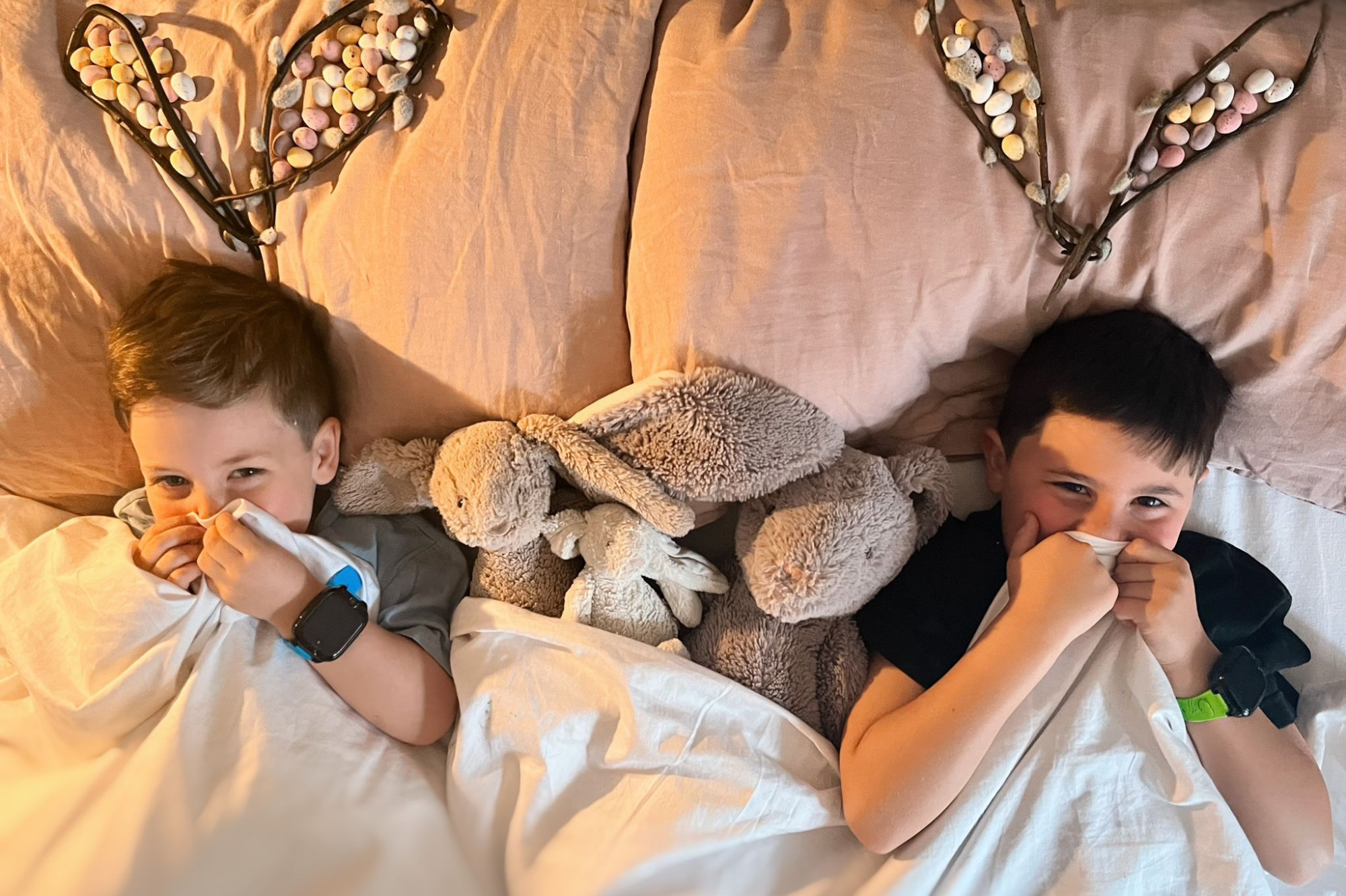 en familie på fire med to børn, der hver har et xplora mobilur. Fra venstre er der en pige med et lyserødt ur, en far, en blond dreng med et blåt ur og en mor yderst til højre.